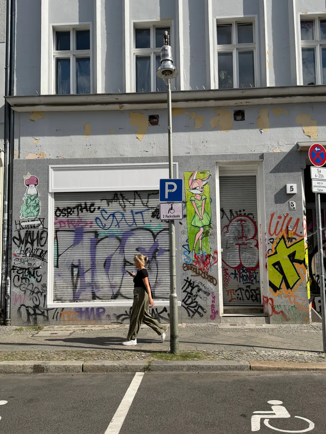 The graffiti-covered shopfront at Eisenbahnstraße 5, with a woman walking past