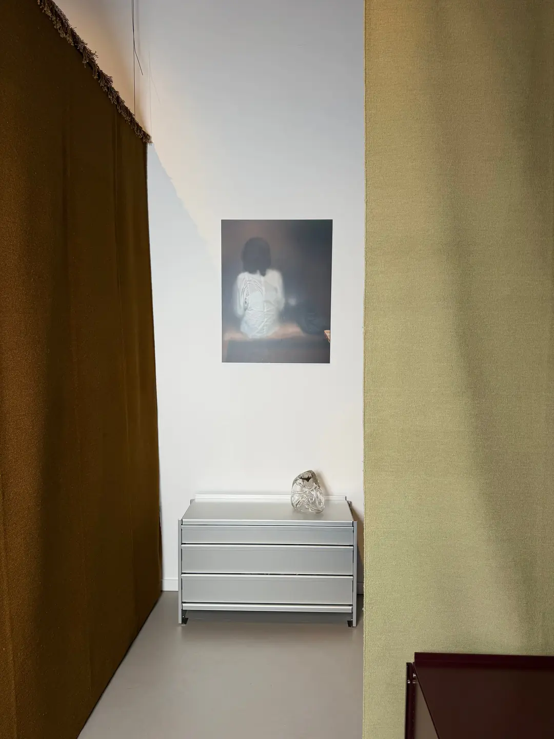 An olive rug hangs beside an aluminium chest of drawers, under a photograph on the studio wall